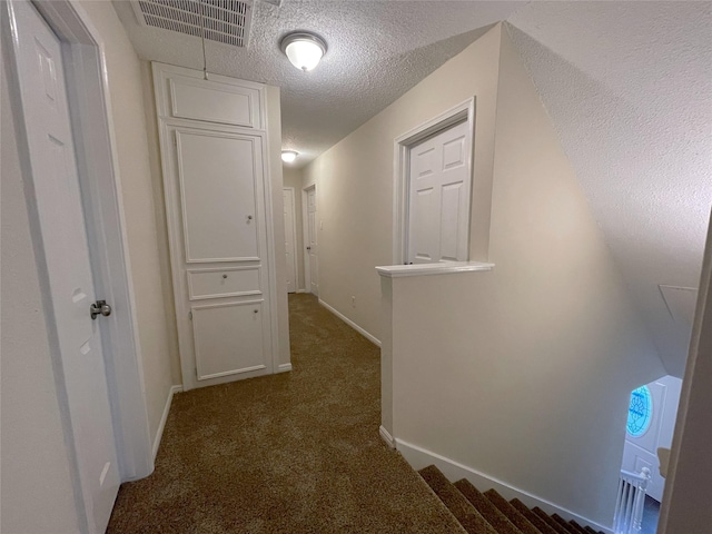 hallway with dark carpet and a textured ceiling