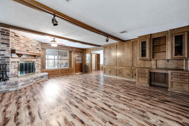 unfurnished living room featuring wooden walls, a fireplace, a textured ceiling, built in desk, and beamed ceiling