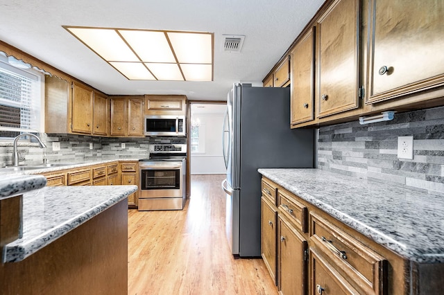 kitchen featuring decorative backsplash, sink, light wood-type flooring, light stone countertops, and stainless steel appliances