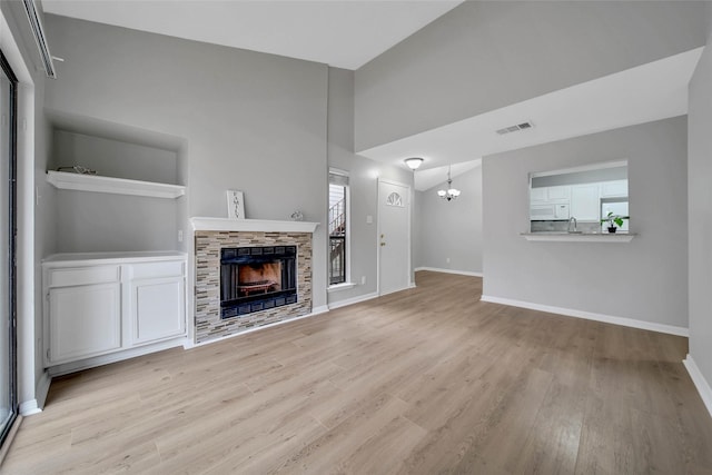 unfurnished living room featuring a stone fireplace, light wood-type flooring, vaulted ceiling, and a notable chandelier