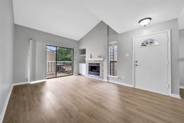 foyer entrance with light hardwood / wood-style floors, vaulted ceiling, and a brick fireplace