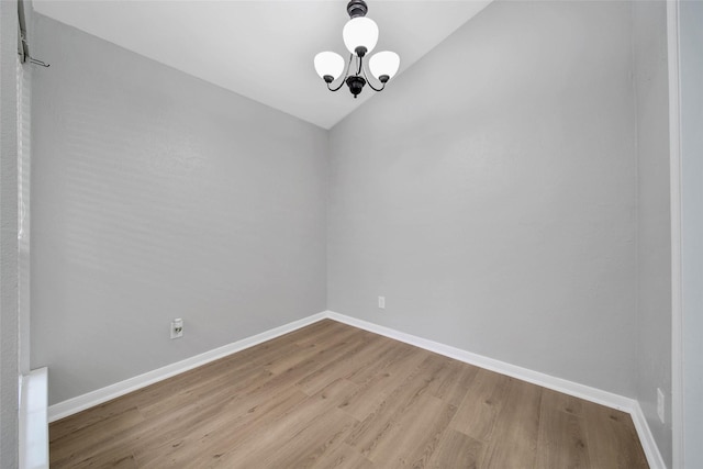 empty room featuring lofted ceiling, light wood-type flooring, and an inviting chandelier