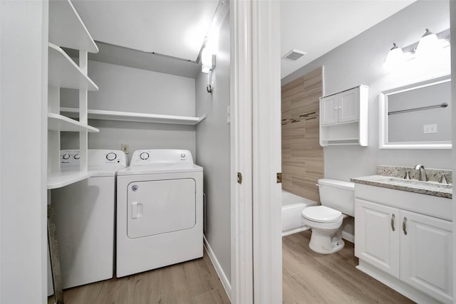 laundry area featuring washing machine and clothes dryer, sink, and light hardwood / wood-style floors