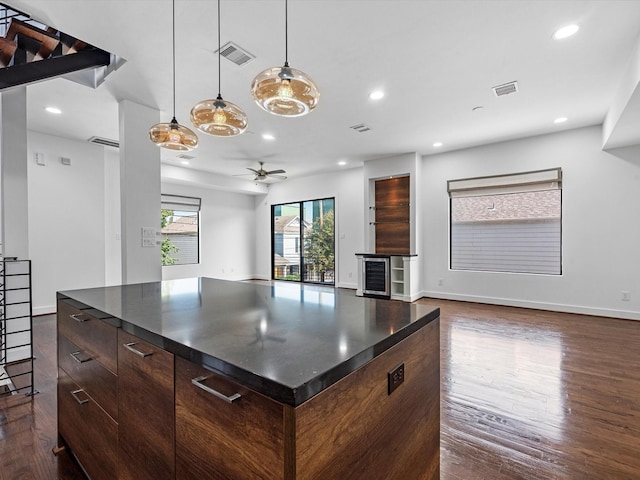 kitchen with ceiling fan, a center island, beverage cooler, dark hardwood / wood-style floors, and dark brown cabinets