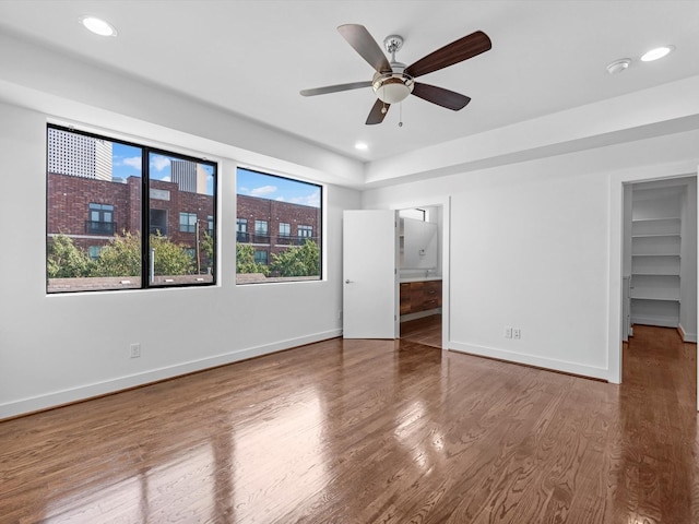 unfurnished bedroom featuring hardwood / wood-style floors, ceiling fan, a spacious closet, and a closet