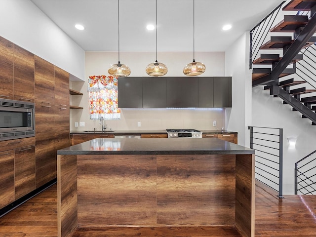 kitchen featuring stove, sink, decorative light fixtures, a center island, and stainless steel microwave