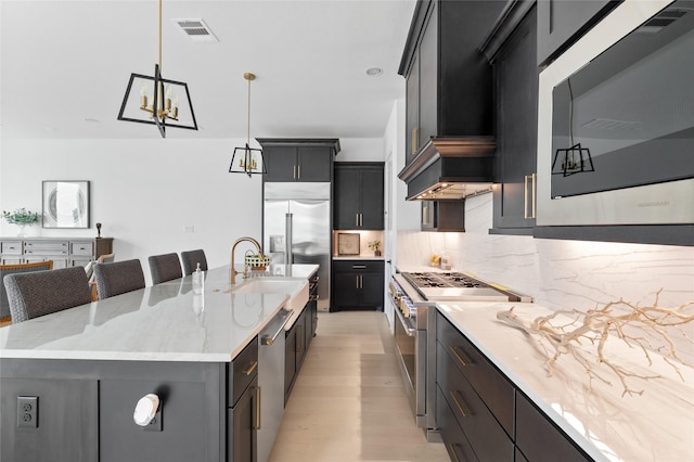 kitchen featuring light stone countertops, tasteful backsplash, pendant lighting, built in appliances, and a large island