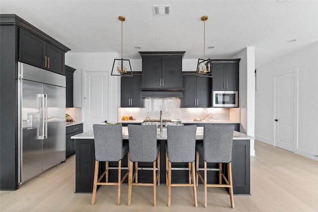 kitchen with pendant lighting, stainless steel appliances, light hardwood / wood-style flooring, and a kitchen island with sink