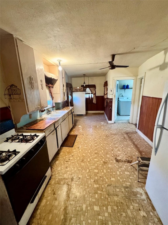 kitchen featuring white appliances, hanging light fixtures, wooden walls, a textured ceiling, and washer / clothes dryer