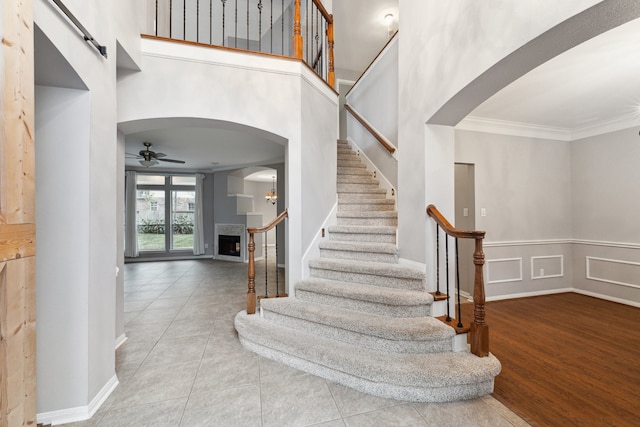 2109 Enchanted Lake Dr, League City, TX 77573 - stairway featuring arched walkways, ornamental molding, a fireplace, ceiling fan, and a high ceiling