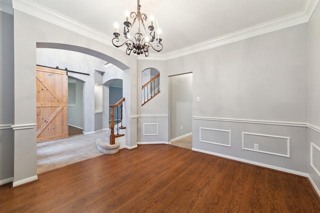 spare room featuring a barn door, crown molding, a chandelier, and hardwood / wood-style flooring