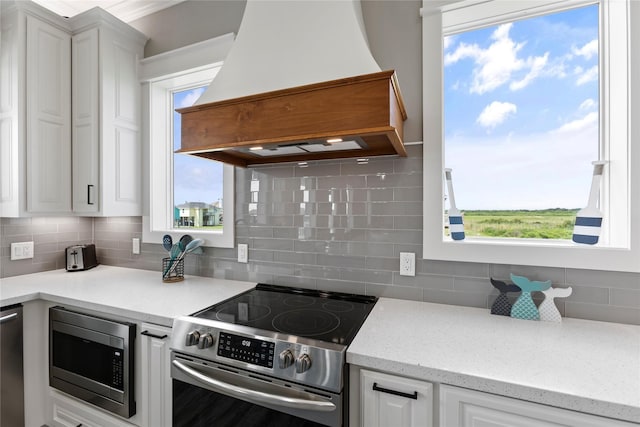 kitchen featuring custom exhaust hood, appliances with stainless steel finishes, tasteful backsplash, light stone counters, and white cabinetry