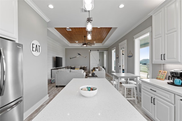 kitchen featuring white cabinetry, tasteful backsplash, a barn door, stainless steel fridge, and decorative light fixtures