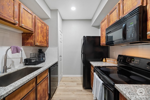 kitchen with sink, light stone counters, light hardwood / wood-style floors, decorative backsplash, and black appliances