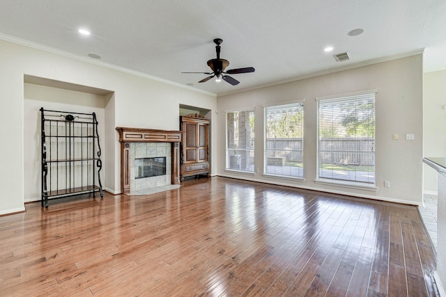 unfurnished living room with a tiled fireplace, crown molding, and wood-type flooring