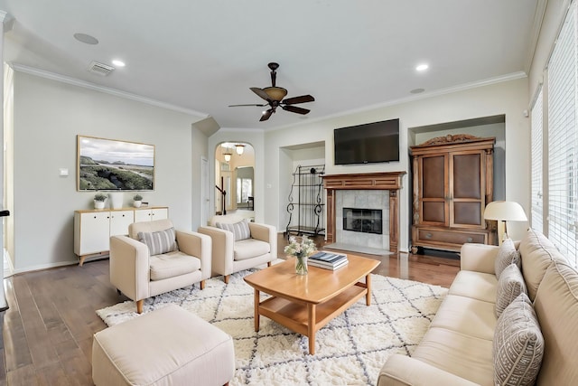 living room with ceiling fan, wood-type flooring, a tile fireplace, and crown molding