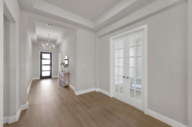 interior space featuring a tray ceiling, hardwood / wood-style floors, an inviting chandelier, and french doors