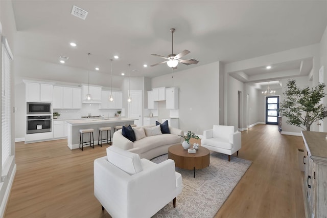 living room featuring ceiling fan with notable chandelier and light hardwood / wood-style flooring