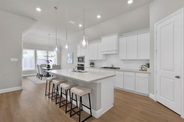 kitchen featuring pendant lighting, stainless steel appliances, a center island with sink, and white cabinets