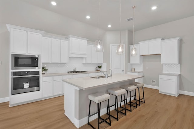 kitchen featuring appliances with stainless steel finishes, a kitchen breakfast bar, pendant lighting, a kitchen island with sink, and white cabinets