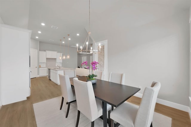 dining area featuring an inviting chandelier, sink, and light hardwood / wood-style flooring