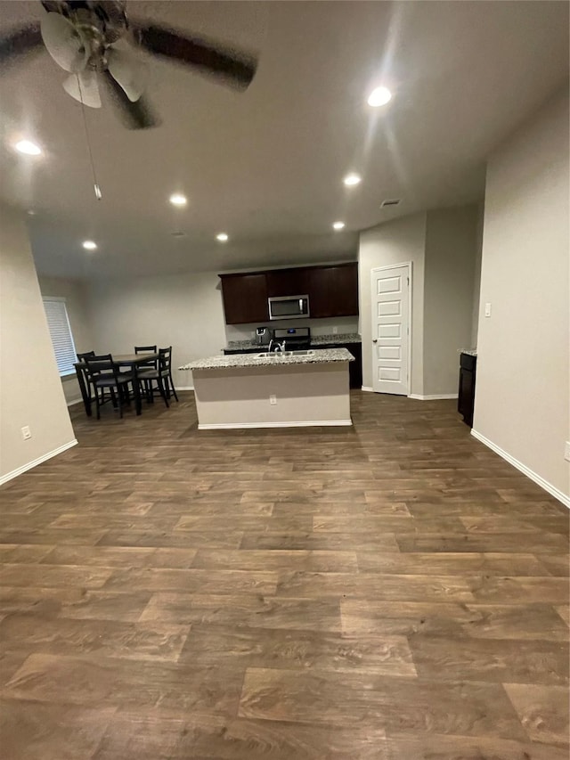 kitchen featuring dark wood-type flooring, light stone countertops, dark brown cabinetry, and a center island with sink