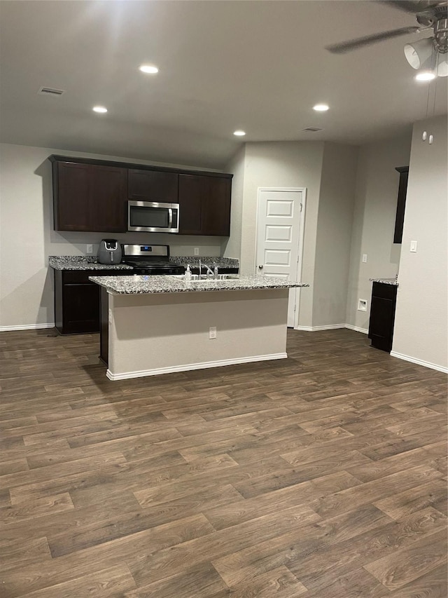 kitchen featuring light stone countertops, dark hardwood / wood-style flooring, stainless steel appliances, and an island with sink