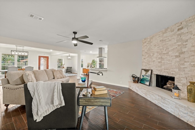 living room with ceiling fan with notable chandelier and a stone fireplace