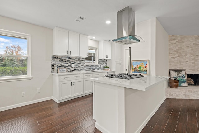 kitchen with light stone countertops, stainless steel gas cooktop, white cabinets, and island range hood