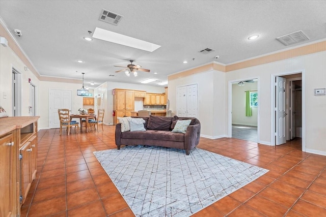 living room featuring a skylight, tile patterned floors, ceiling fan, and ornamental molding