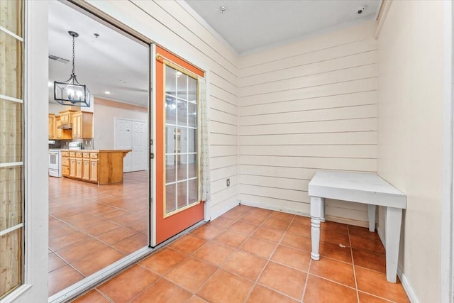 doorway to outside with a chandelier, wooden walls, and light tile patterned flooring