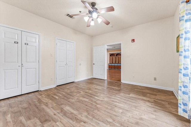 unfurnished bedroom with two closets, light hardwood / wood-style flooring, and ceiling fan