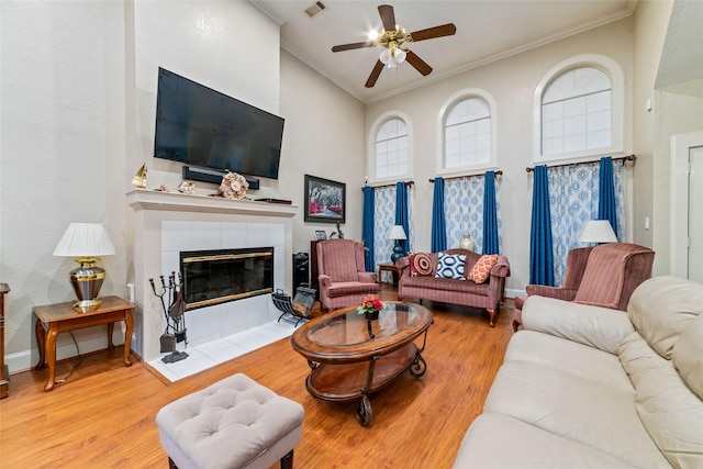 living room featuring ceiling fan, crown molding, a tile fireplace, and light hardwood / wood-style flooring