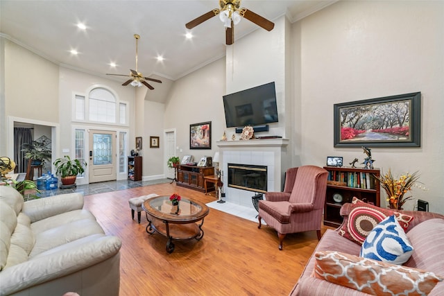 living room featuring light hardwood / wood-style flooring, ceiling fan, ornamental molding, a towering ceiling, and a tiled fireplace