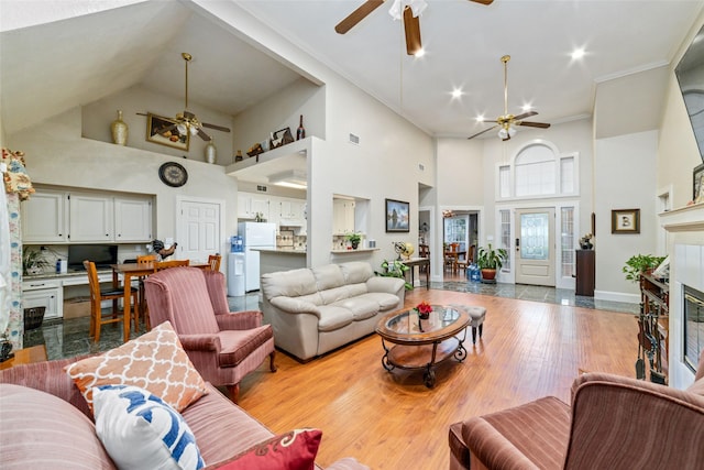 living room with a tile fireplace, a towering ceiling, light hardwood / wood-style floors, and ornamental molding