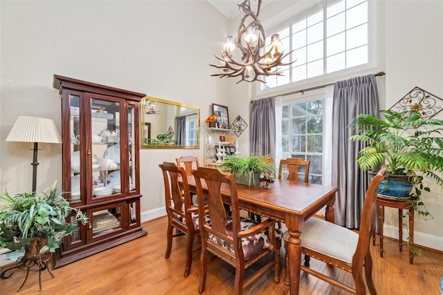 dining area with a chandelier, light wood-type flooring, and a towering ceiling