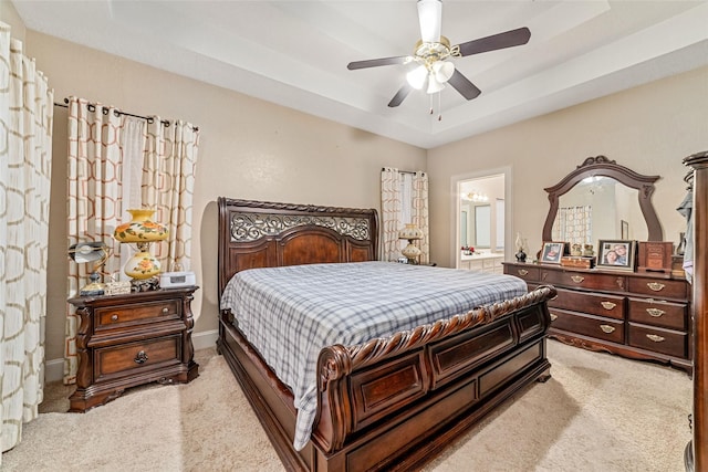 carpeted bedroom featuring ensuite bath, ceiling fan, and a tray ceiling