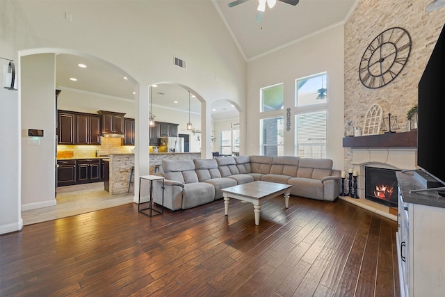 living room with ceiling fan, high vaulted ceiling, crown molding, a fireplace, and hardwood / wood-style flooring