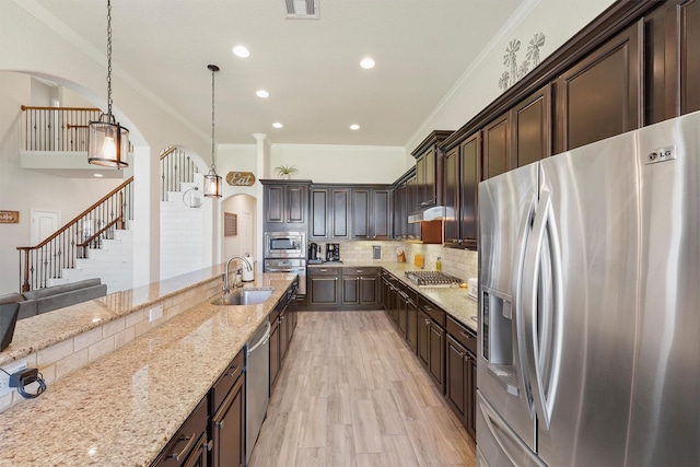 kitchen featuring appliances with stainless steel finishes, light stone counters, dark brown cabinetry, sink, and pendant lighting