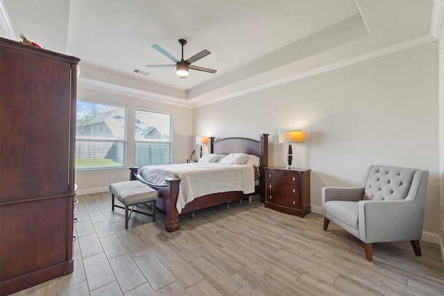 bedroom with light wood-type flooring, a raised ceiling, ceiling fan, and ornamental molding