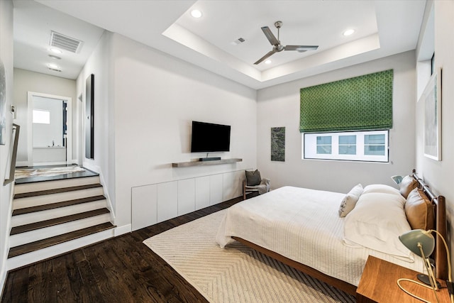 bedroom with ceiling fan, multiple windows, dark hardwood / wood-style floors, and a tray ceiling