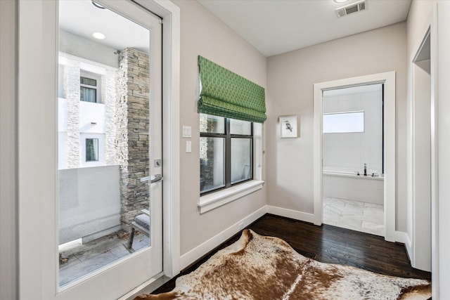 bathroom featuring a wealth of natural light, tiled tub, and wood-type flooring