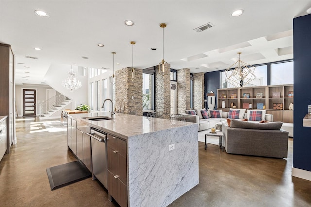 kitchen with light stone countertops, a notable chandelier, concrete floors, a large island with sink, and sink