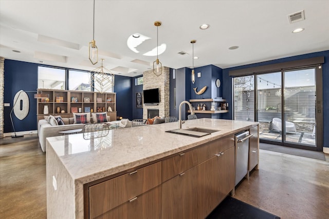 kitchen featuring sink, decorative light fixtures, an island with sink, concrete floors, and a stone fireplace