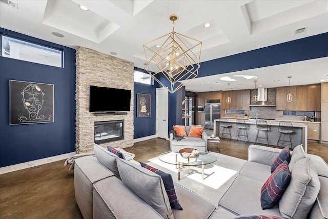 living room featuring an inviting chandelier, concrete flooring, coffered ceiling, and a stone fireplace