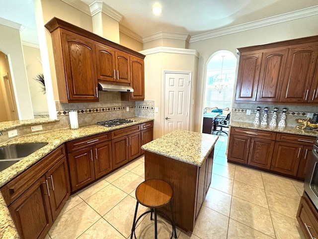 kitchen with tasteful backsplash, light stone counters, ornamental molding, a kitchen island, and stainless steel gas stovetop