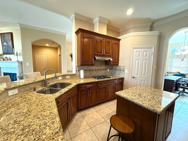 kitchen featuring stainless steel gas stovetop, sink, light stone countertops, a notable chandelier, and a kitchen bar