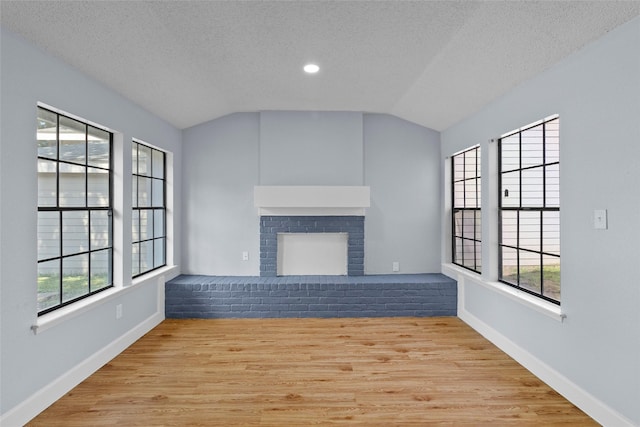 unfurnished living room featuring a fireplace, a textured ceiling, light hardwood / wood-style flooring, and vaulted ceiling