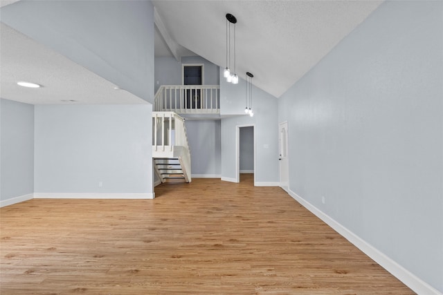 unfurnished living room featuring light wood-type flooring, a textured ceiling, and high vaulted ceiling