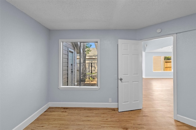 empty room featuring a textured ceiling, light hardwood / wood-style flooring, and a healthy amount of sunlight